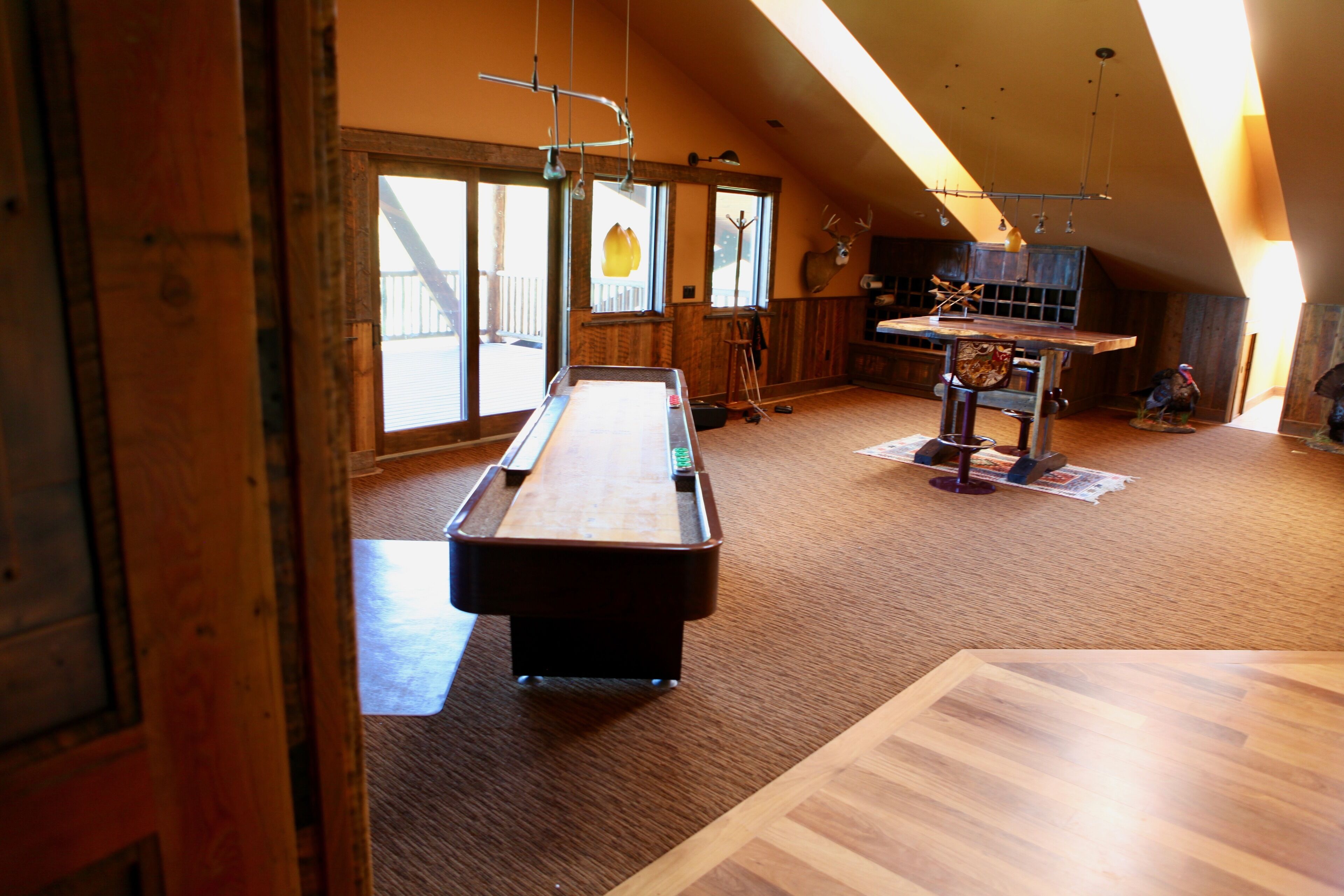 A spacious room with a pool table, wooden flooring, large windows, and a high ceiling.