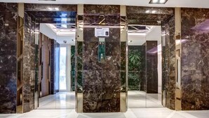 Un moderno ascensor con paredes de mármol y una pantalla digital, que da acceso a un espacio interior bien iluminado.
