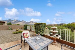 Un patio exterior con una mesa y sillas, una fuente decorativa y vistas a montañas.
