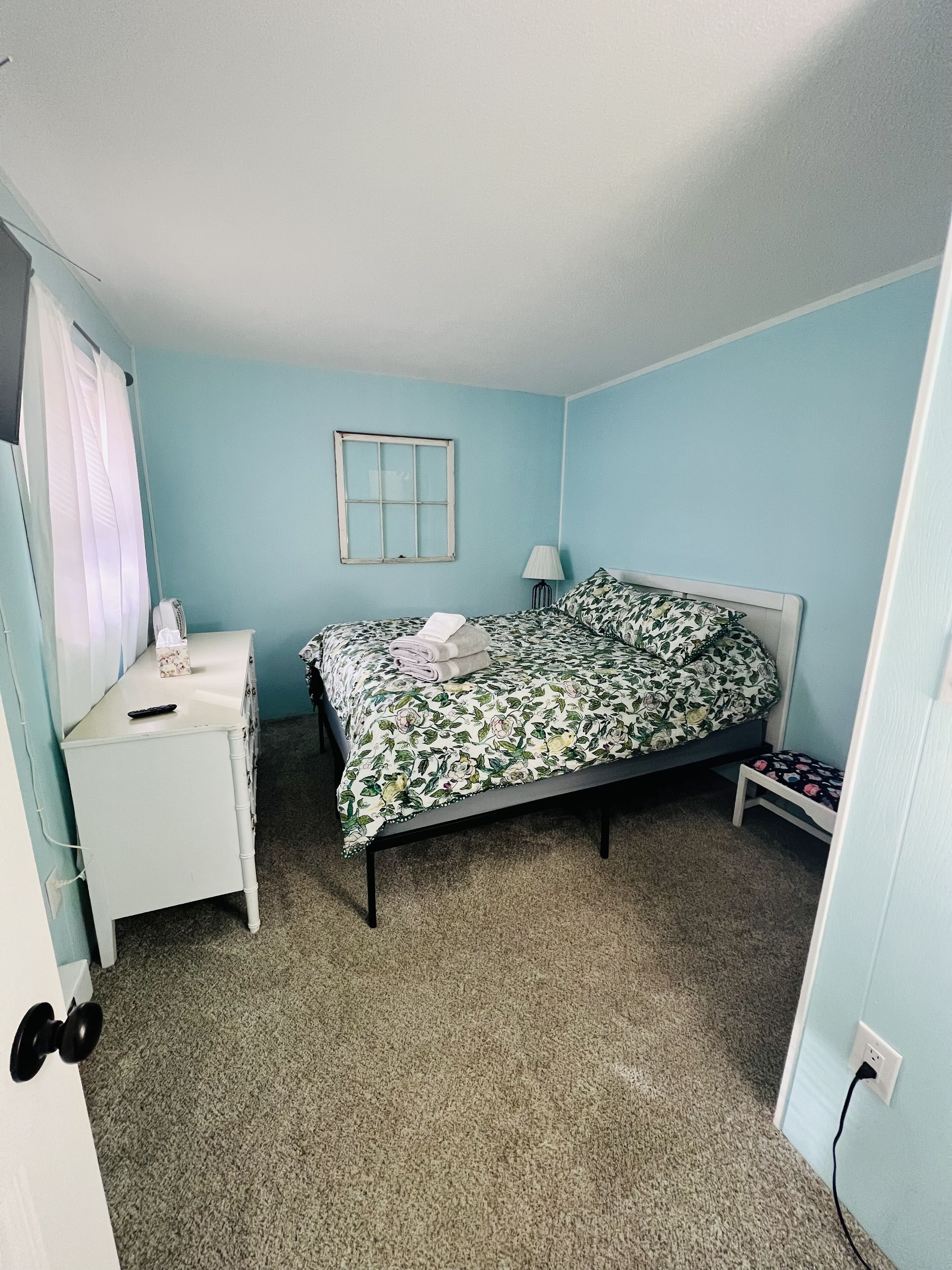 A bedroom with a bed, a bedside table, a lamp, and a window.