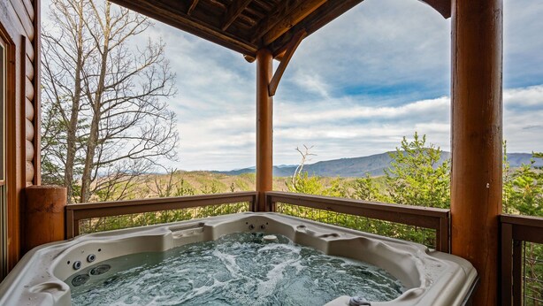 Un jacuzzi con terraza de madera y una vista panorámica de montañas y árboles.