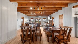 Un comedor amplio con una larga mesa de madera y sillas, paredes blancas con paneles y un techo de madera con vigas a la vista.