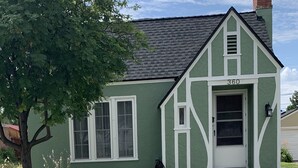 Een groen huis met een witte deur en ramen, een schoorsteen en het nummer '360' op de gevel.