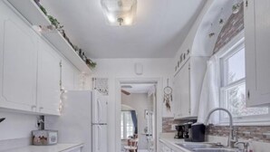 Een kleine keuken met witte kastjes, een koelkast en een wastafel.