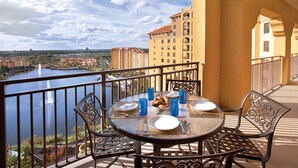 A balcony with a table set for two, overlooking a body of water and a cityscape.
