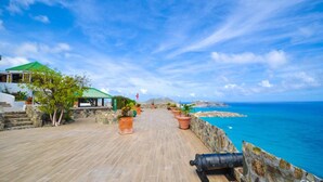 A coastal walkway with a stone wall, potted plants, and a building with a green roof. - 🌴Joy Estate by IRE Vacations - Expansive Property with Amazing Views ☀️ (Cay Hill)
