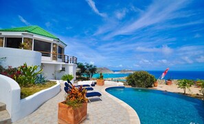 Une maison moderne avec une piscine, une vue sur l’océan et un ciel dégagé.