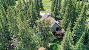 A cabin surrounded by dense forest, with a deck and a chimney.