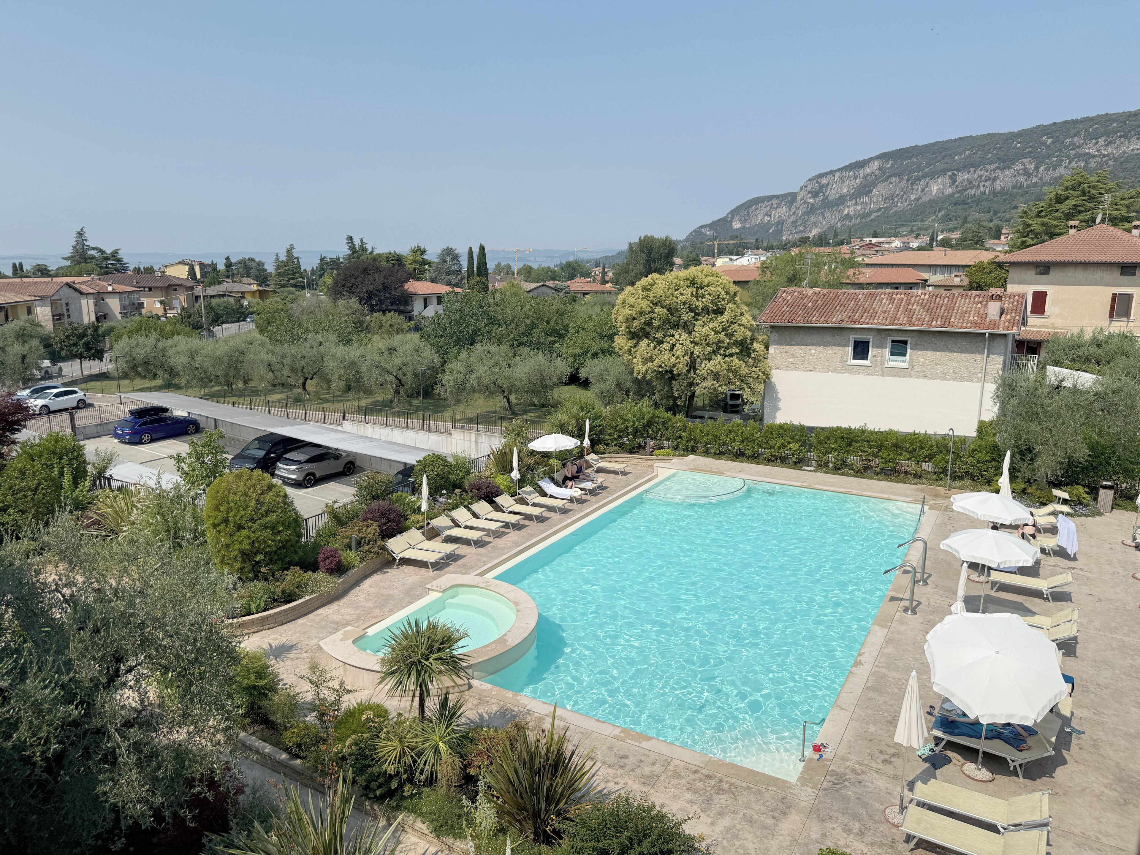 Une piscine entourée de verdure et d’immeubles d’habitation, avec des chaises longues et des parasols.