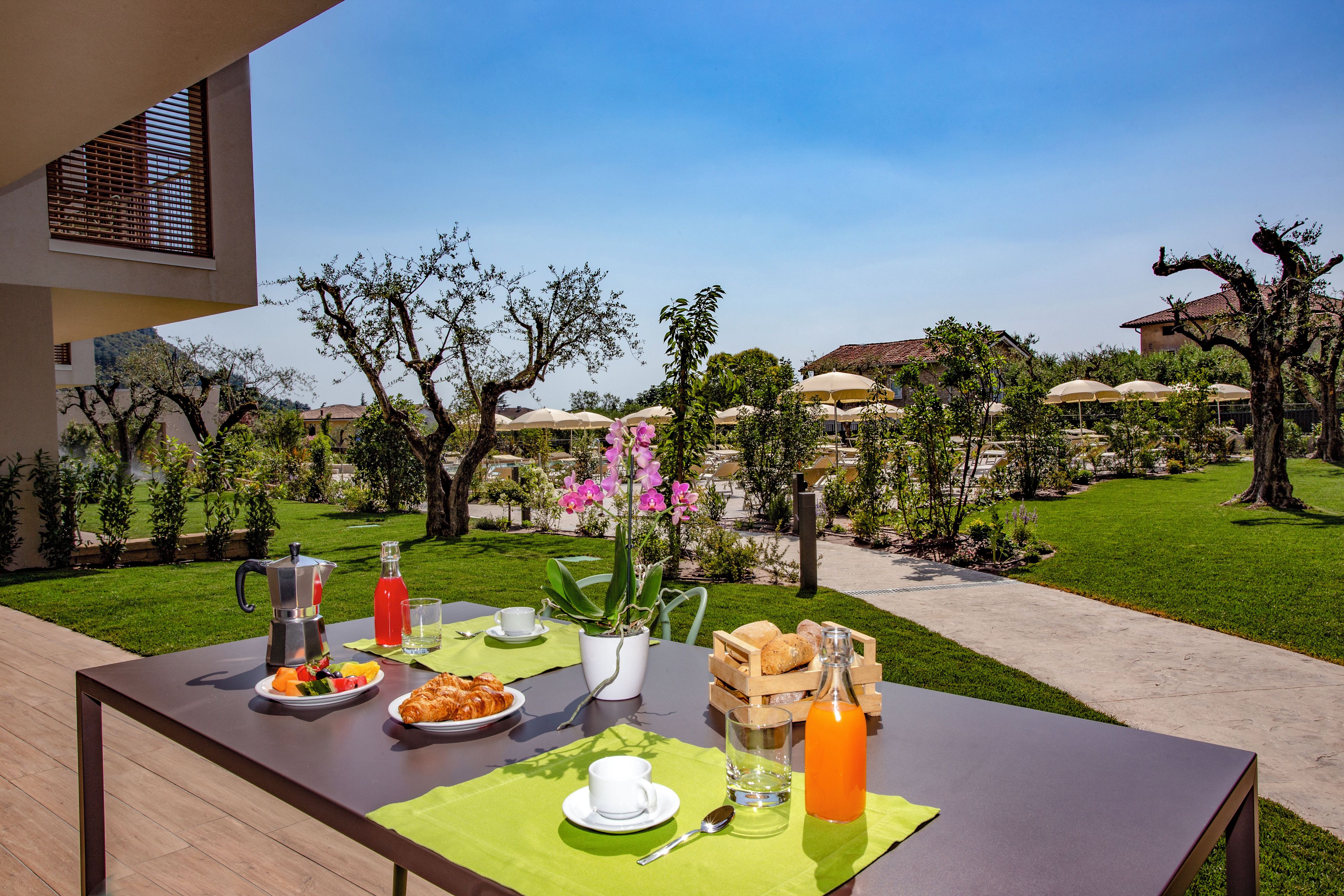 Un área de comedor al aire libre con una mesa dispuesta para el desayuno, incluyendo croissants, fruta y bebidas.