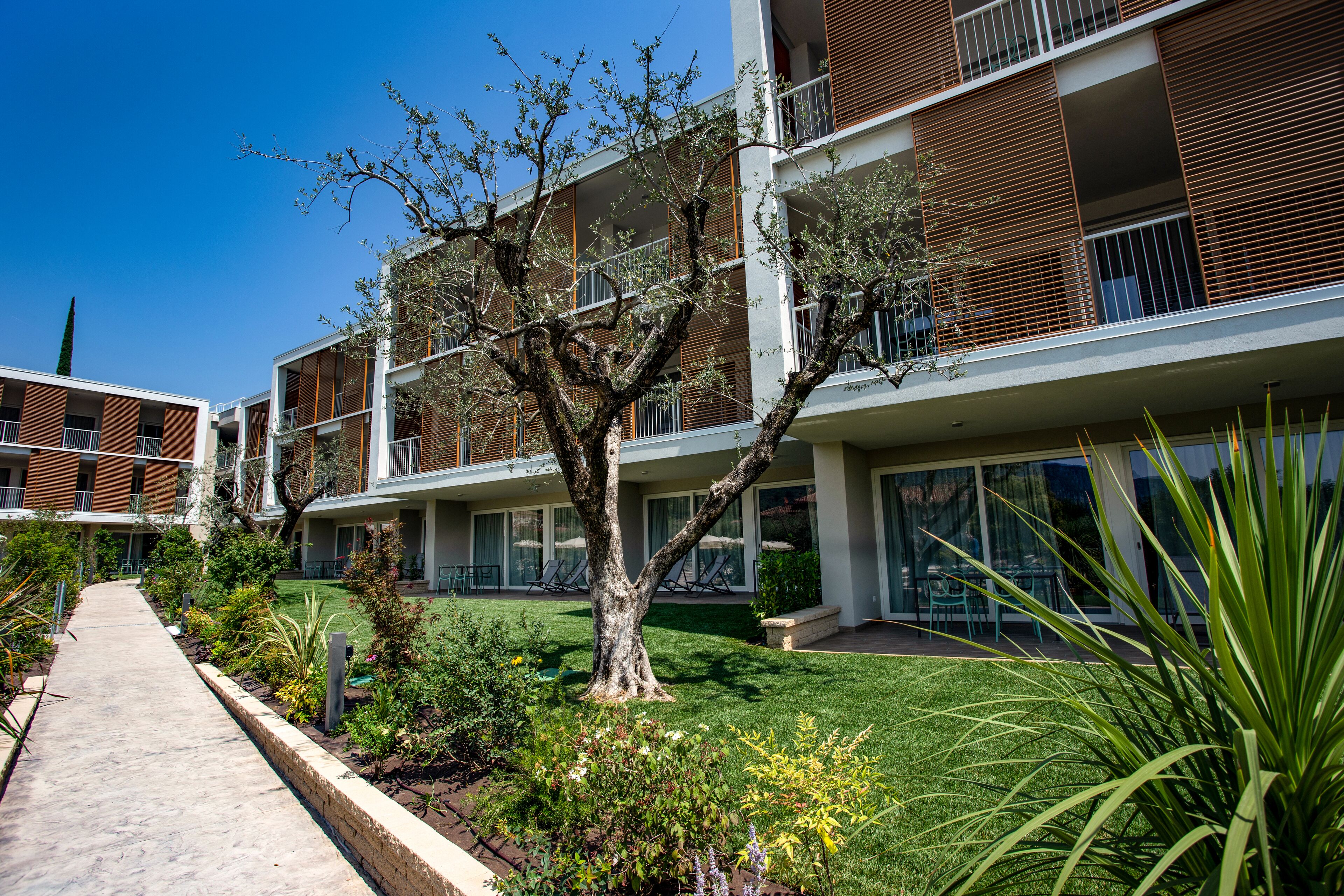 A modern apartment building with balconies, a well-maintained lawn, and a clear sky.