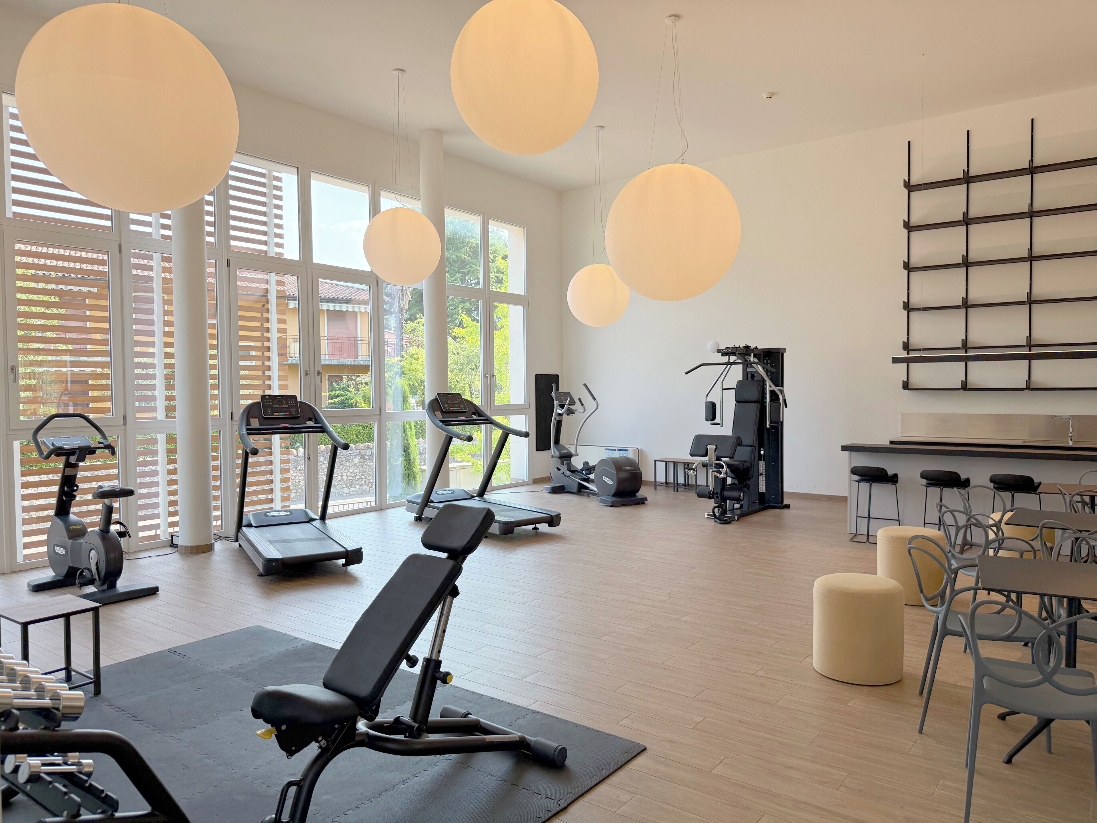 A modern gym with exercise equipment, large windows, and a dining area.