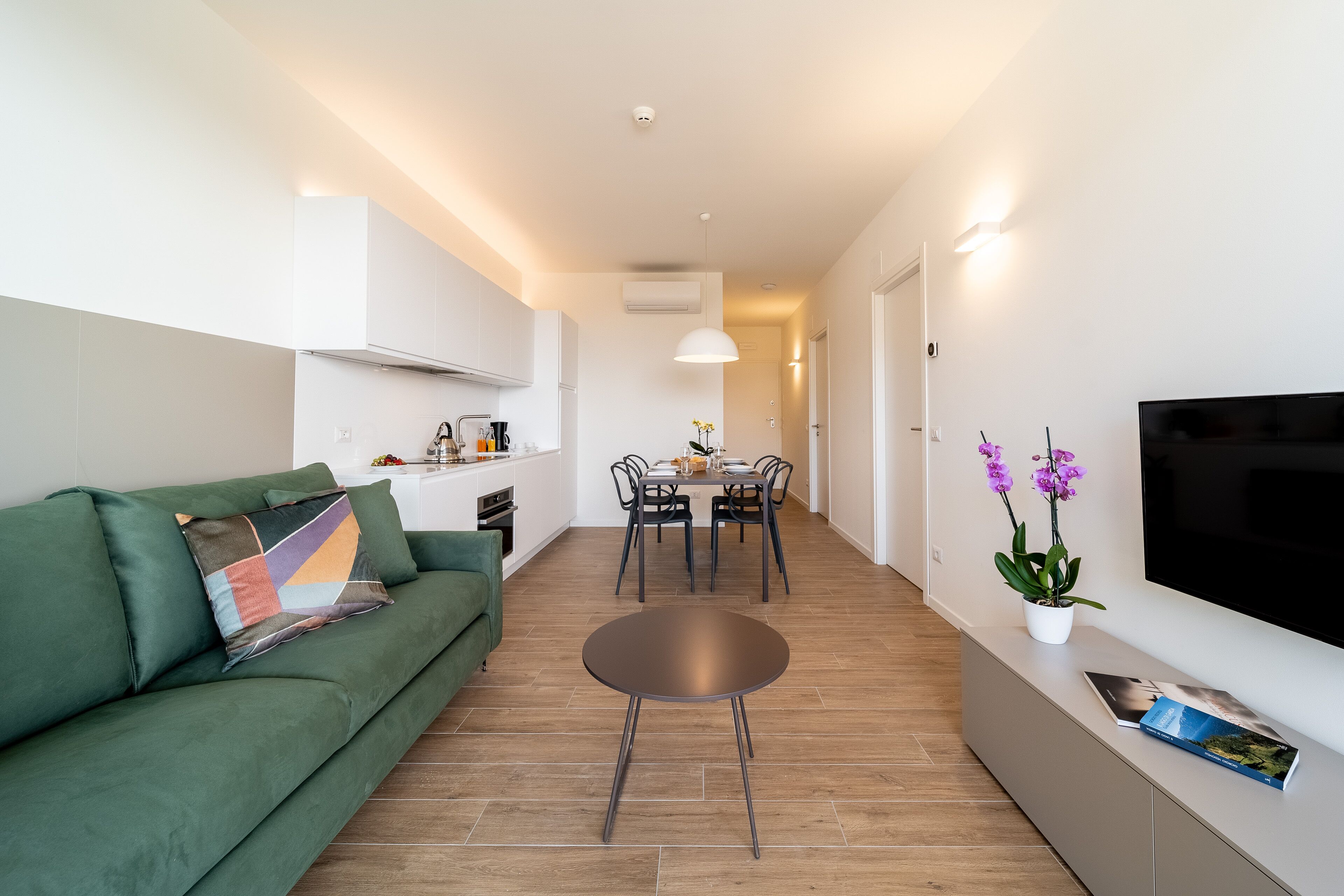 A modern living room with a green sofa, a round coffee table, and a dining area with a table and chairs.