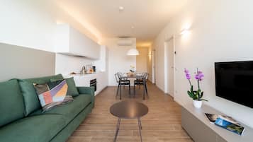 A modern living room with a green sofa, a round coffee table, and a dining area with a table and chairs.