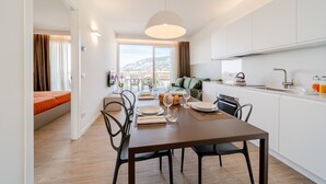 Een moderne keuken met witte kastjes, een eethoek met een tafel gedekt voor twee personen, en uitzicht op de stad door grote ramen.