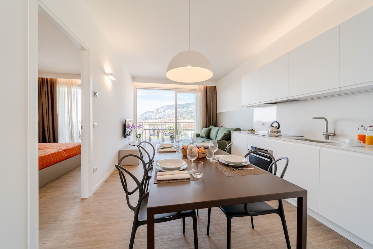 Eine moderne Küche mit weißen Schränken, ein Essbereich mit Tisch für zwei Personen und Blick auf die Stadt durch große Fenster.