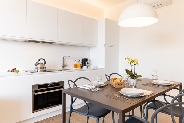 Una cocina moderna con armarios blancos, horno empotrado y comedor con mesa para dos.