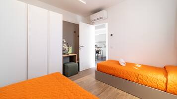 A modern bedroom with two beds, a wardrobe, a kitchenette, and an open door leading to a dining area.