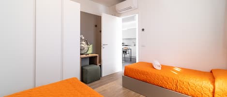 Un dormitorio moderno con dos camas, un armario, una kitchenette y una puerta abierta que da a un comedor.