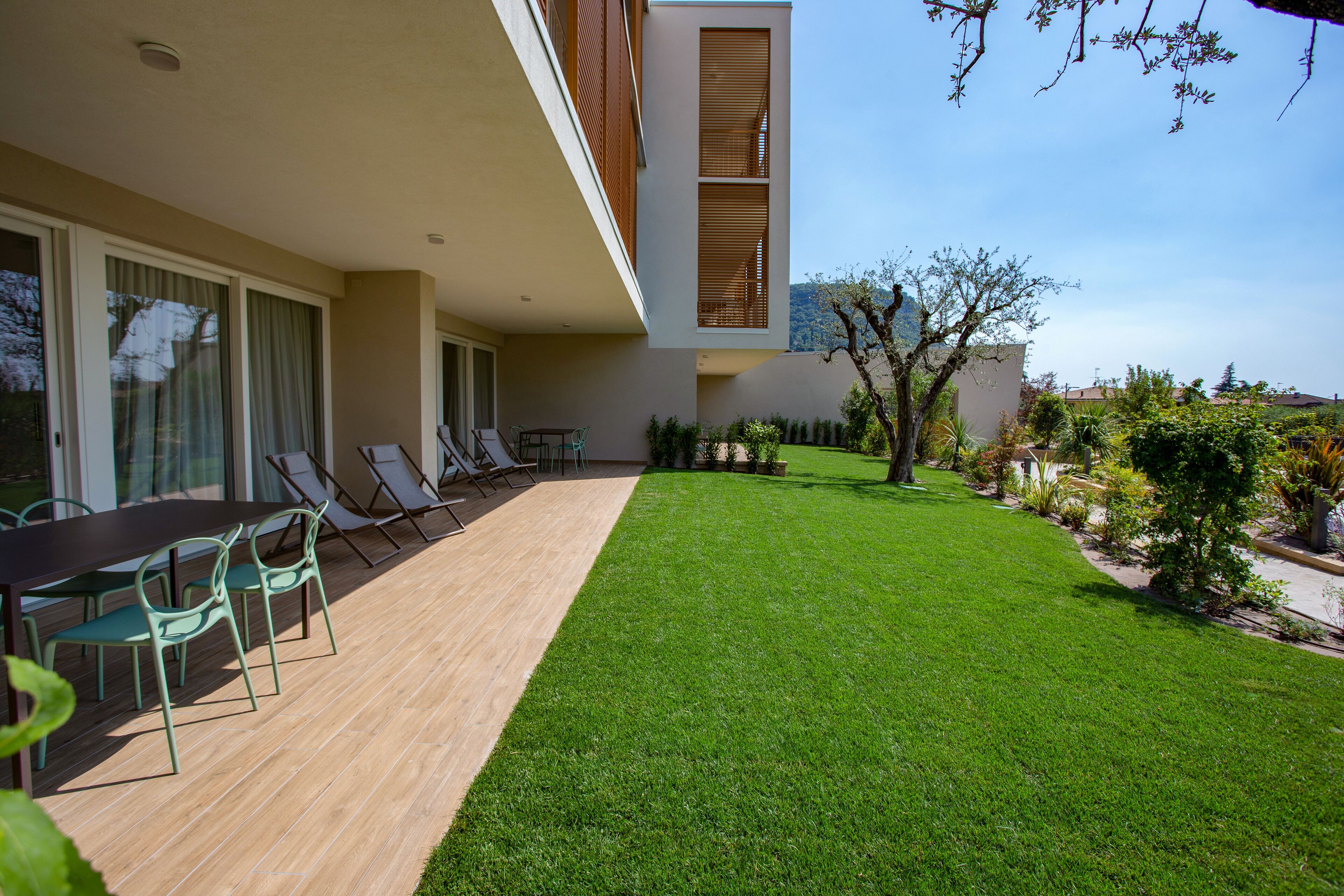 Une terrasse extérieure moderne, dotée d’une plateforme en bois, d’une table à manger avec des chaises et d’une pelouse bien entretenue.