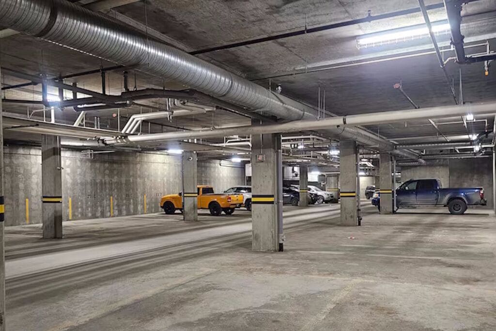 A multi-level parking garage with concrete pillars, overhead pipes, and vehicles parked.
