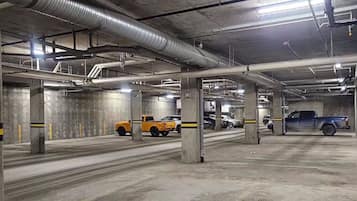 A multi-level parking garage with concrete pillars, overhead pipes, and vehicles parked.