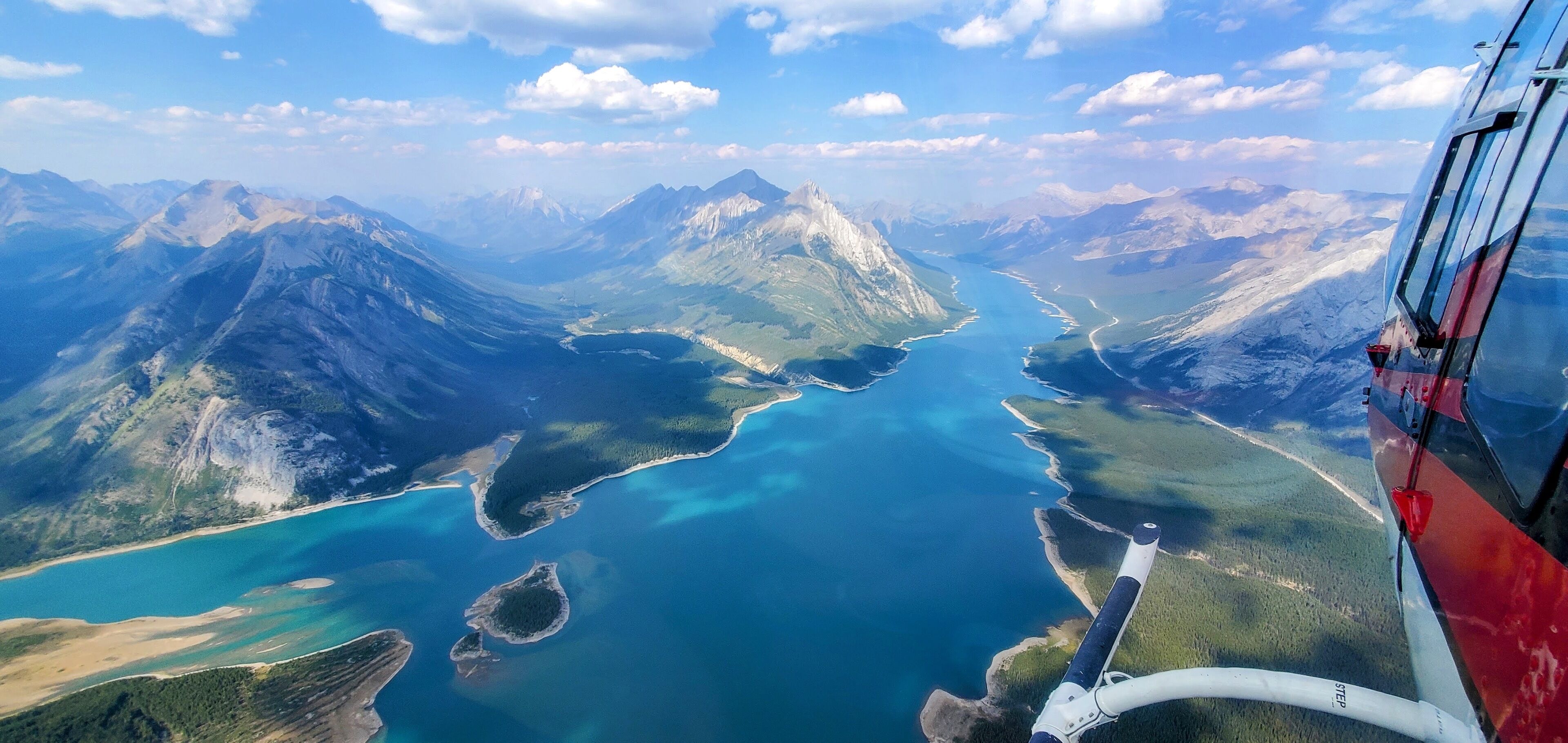 Vue aérienne, prise depuis un hélicoptère, d’un paysage montagneux avec une rivière, un ciel dégagé et l’arrière d’un hélicoptère.