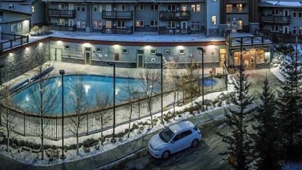 Un hotel de varios pisos con piscina, rodeado de montañas nevadas.