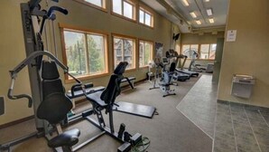 Un gimnasio con diversos equipos de ejercicio, amplias ventanas y suelo de baldosas.
