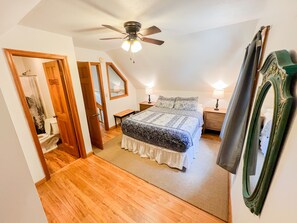 A bedroom with a bed, a ceiling fan, a nightstand, a mirror, and a door leading to a bathroom. - RIVER FRONT HOUSE INSIDE THE COOSAWATTEE RESORT (Ellijay)