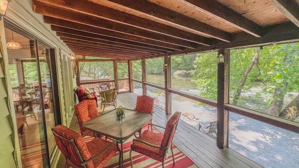 Een overdekt terras met een tafel en stoelen, met uitzicht op een rivier.
