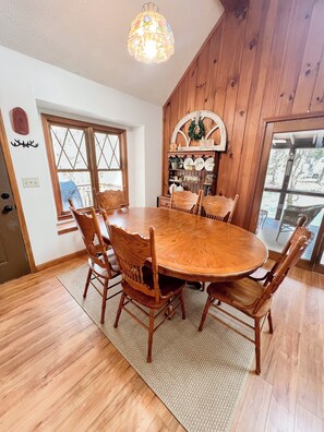 A dining room with a wooden table and chairs, a chandelier, and a window with a view. - RIVER FRONT HOUSE INSIDE THE COOSAWATTEE RESORT (Ellijay)