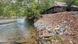 Een vakantiehuisje aan de rivier met een houten terras en een stenen steunmuur.