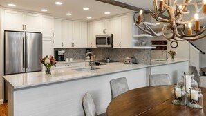 A modern kitchen with white cabinets, stainless steel appliances, and a large island with seating. - Montaneros 410 - 3 Bedroom Diamond (Vail)
