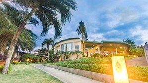 A modern building with a curved roof, surrounded by well-maintained greenery and palm trees. - The Park - Silang (Silang)