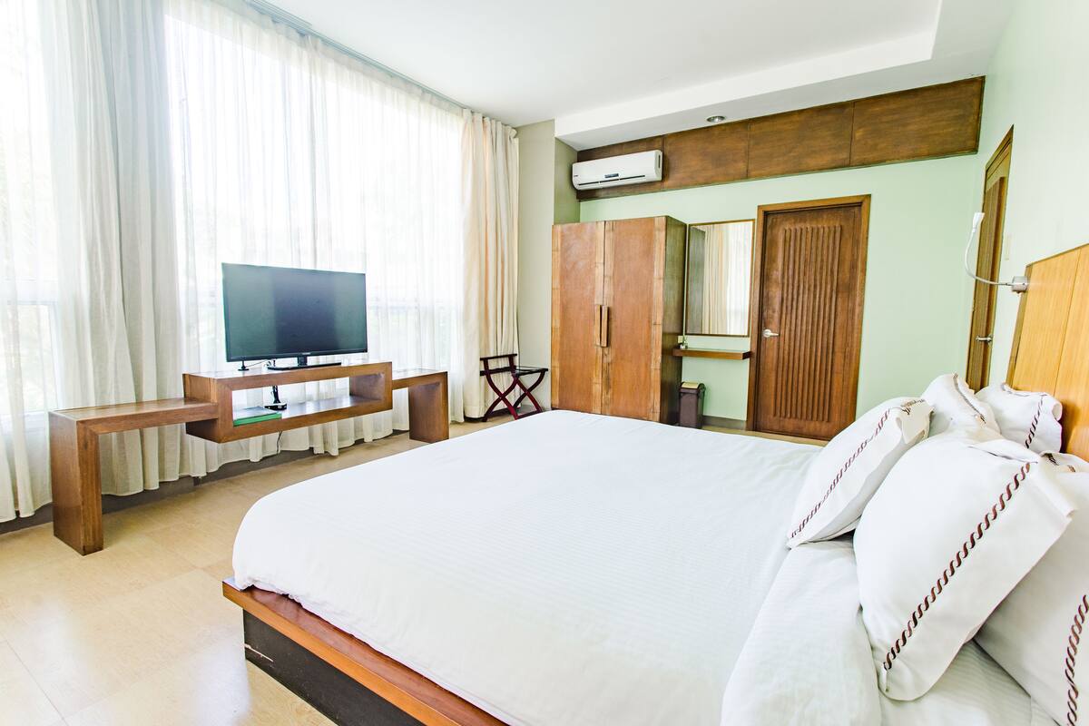 A hotel room with a large bed, a TV on a wooden stand, a wardrobe, and a mirror.