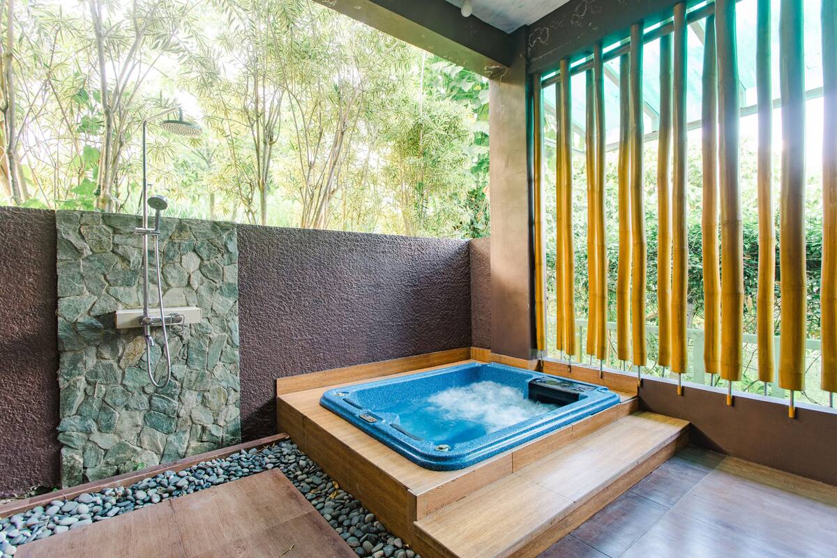 A spa area with a hot tub, stone wall, and a view of greenery through a window.