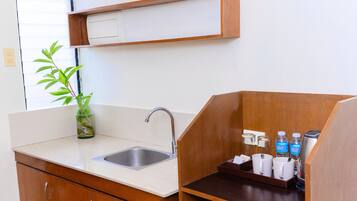 Cocina compacta con lavamanos, armarios de madera, encimera y estante con artículos de tocador.