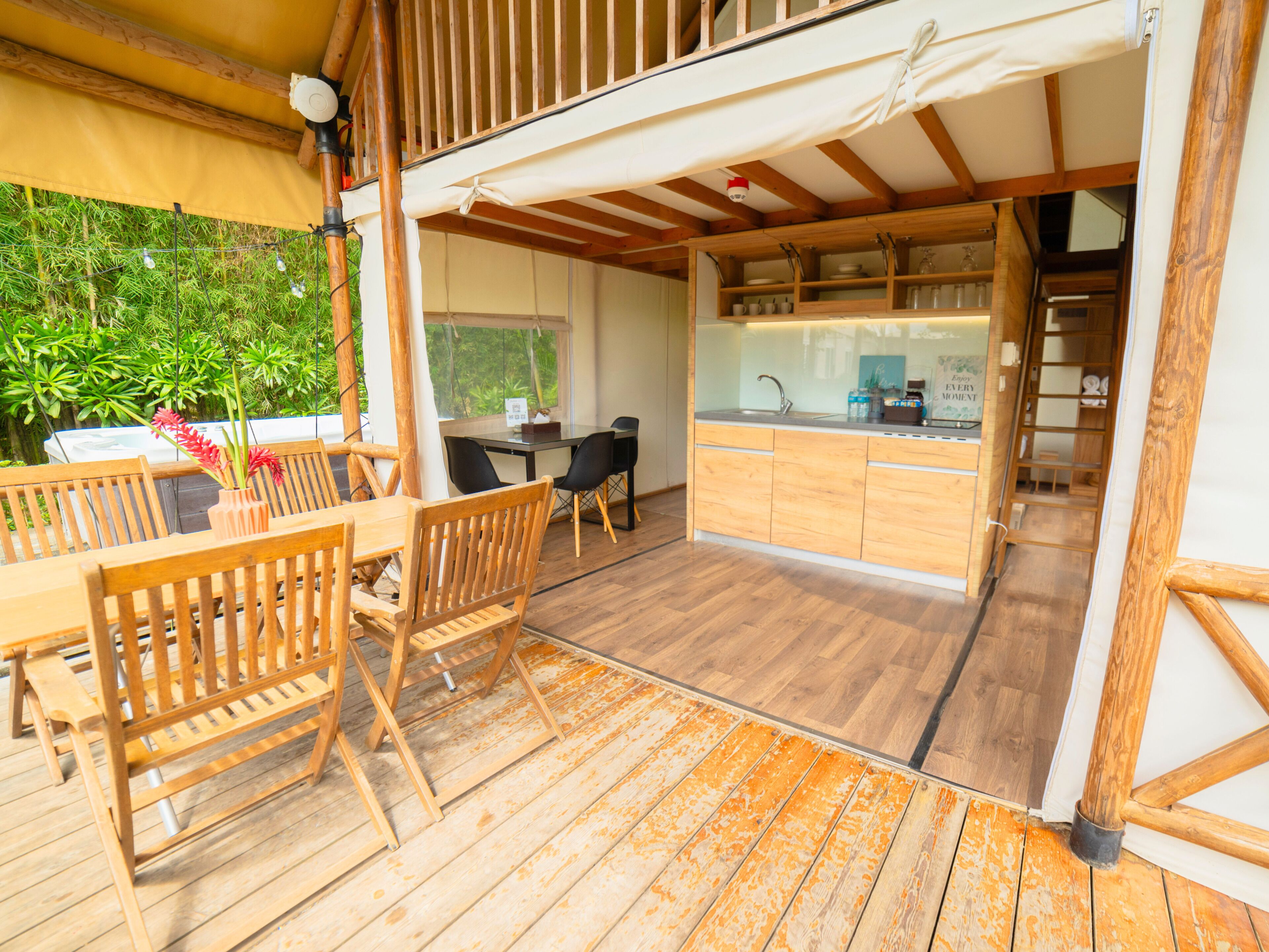 Un espacio habitable de concepto abierto con comedor de madera, cocina con cerramiento de vidrio y vistas a la vegetación.