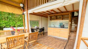 Un espacio habitable de concepto abierto con comedor de madera, cocina con cerramiento de vidrio y vistas a la vegetación.