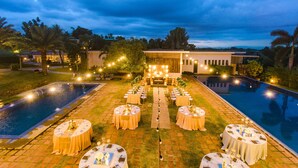 A poolside event setup with round tables, chairs, and a central seating area, surrounded by a pool and a building in the background. - The Park - Silang (Silang)