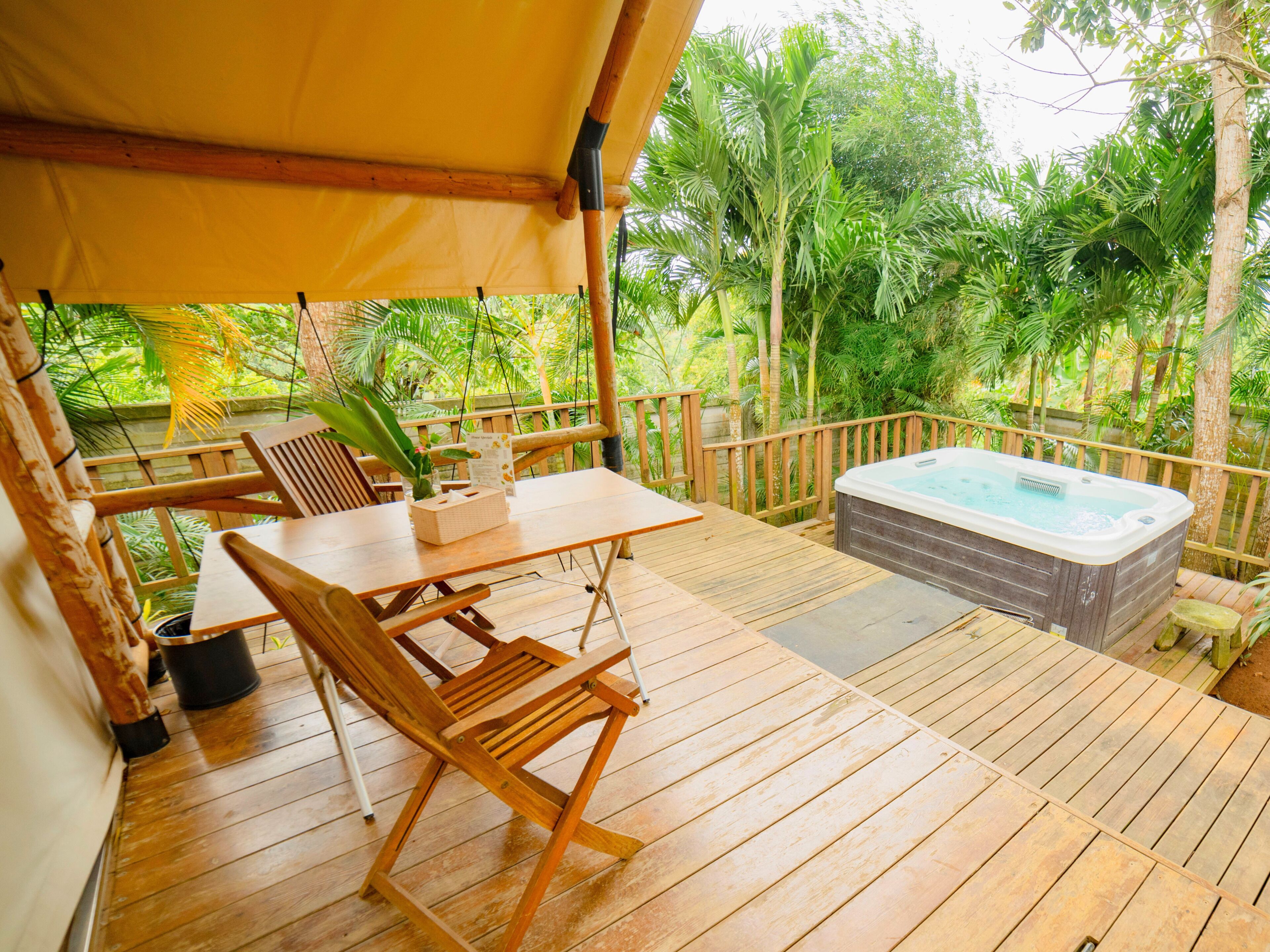 A wooden deck with a hot tub, a table, and chairs.
