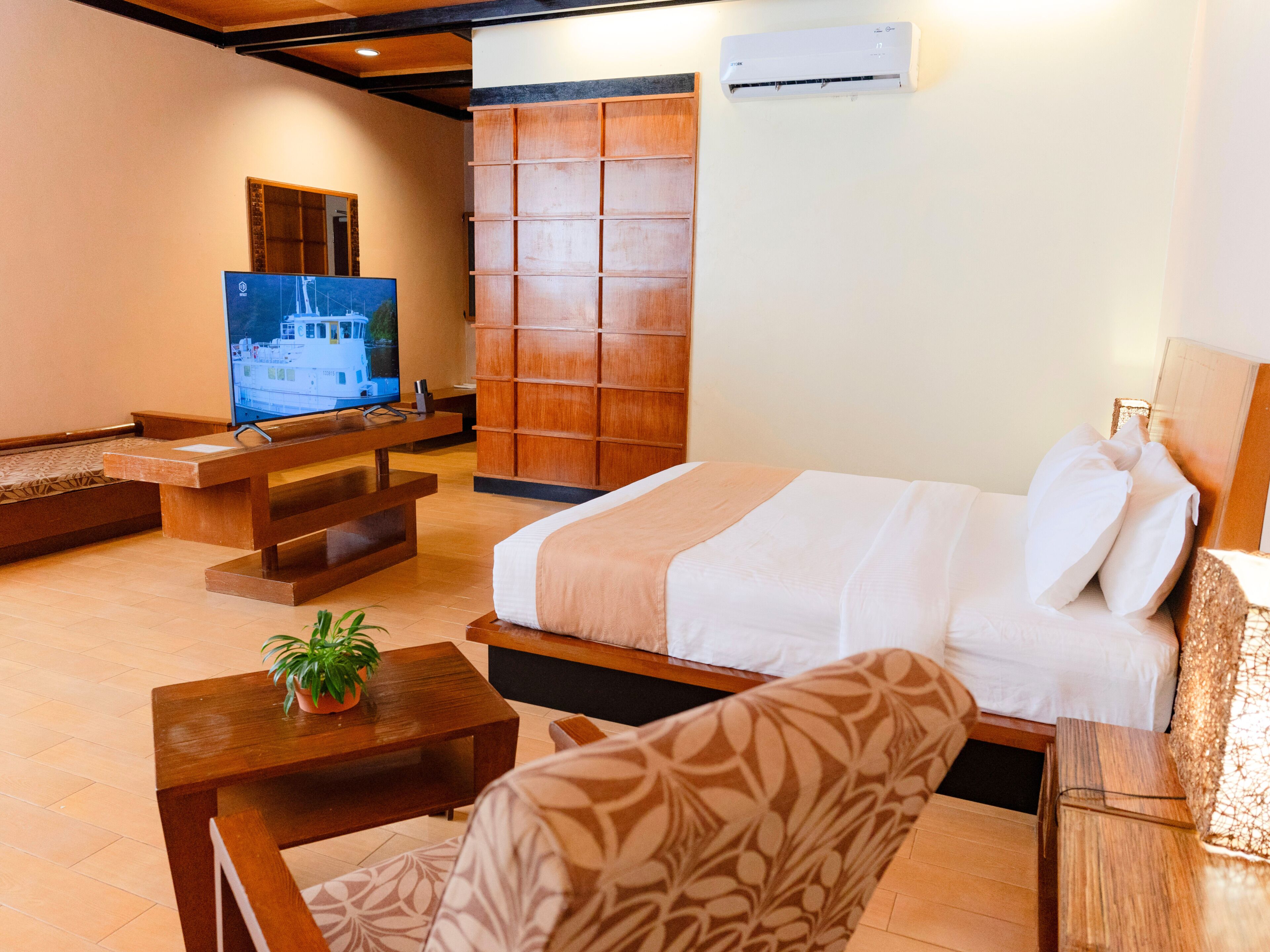 A hotel room with a bed, a television, a wooden cabinet, and a small table with a plant.