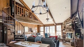 Un salón espacioso con techo alto, una escalera de madera y una araña.