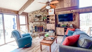 Un salón amplio con pisos de madera, un ventilador de techo, una pared de piedra y un televisor.