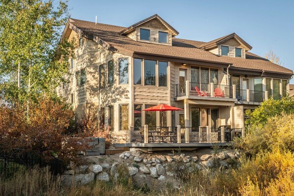 A two-story house with a stone facade, large windows, and a balcony with red chairs.