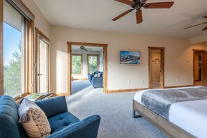 A bedroom with a large bed, a blue sofa, and a ceiling fan.