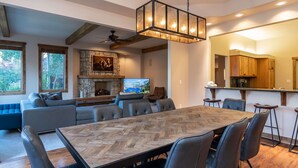 Un salón espacioso con una gran mesa de comedor de madera en diseño espiga, asientos cómodos, chimenea de piedra y una cocina con armarios de madera.