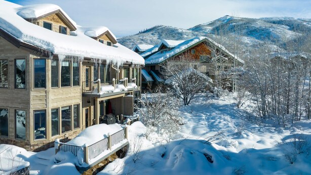 Un edificio cubierto de nieve con múltiples ventanas y un balcón, rodeado de árboles nevados y montañas.