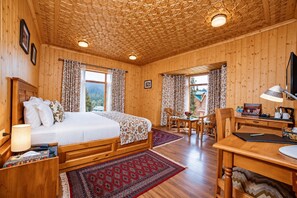A wooden cabin with a bed, desk, and chairs, featuring a patterned ceiling and large windows. - Shaw Inn (Baramula)